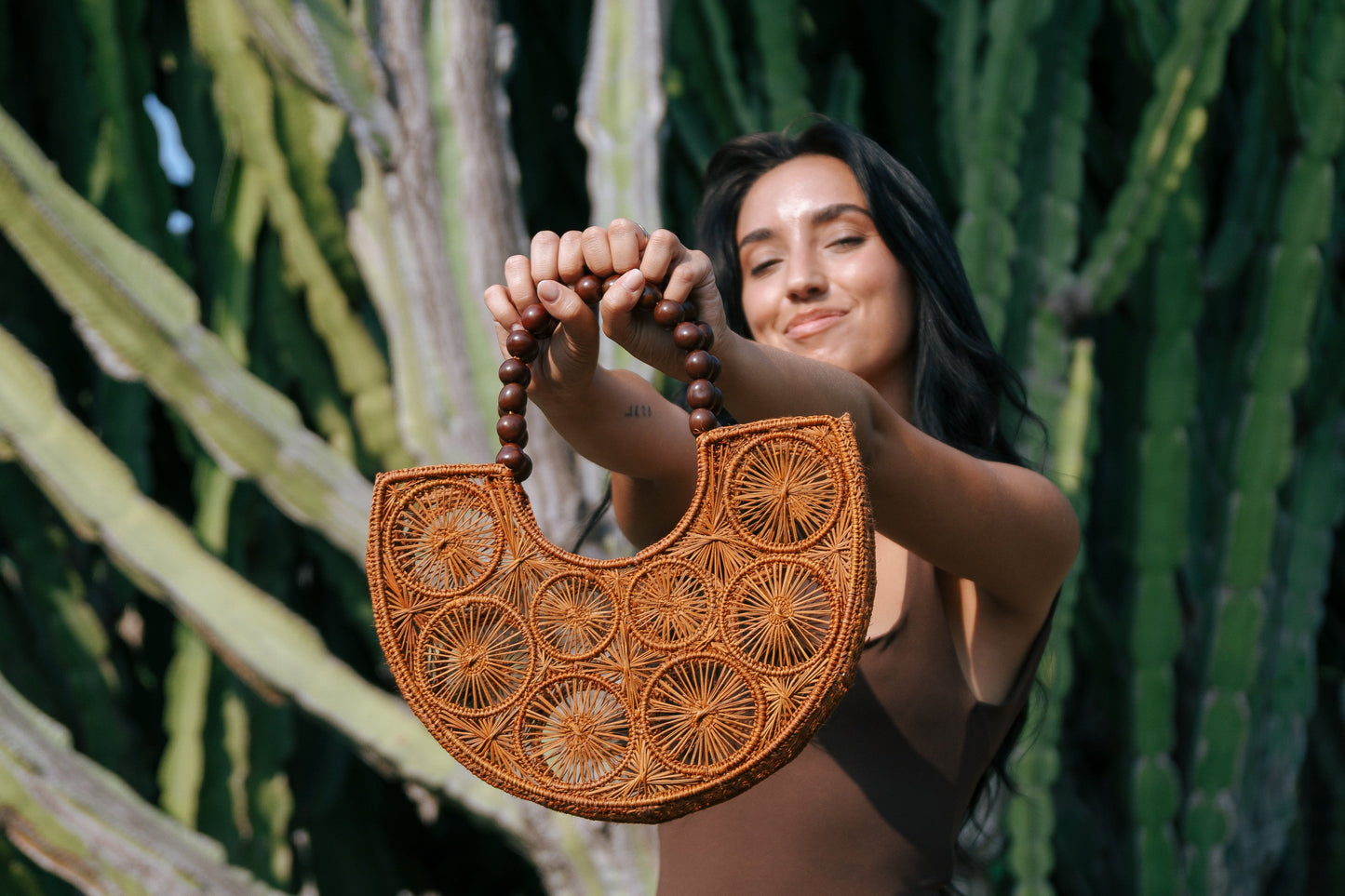 Woman holding a woven handbag in front of cactus