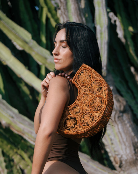 Woman wearing a brown swimsuit with a decorative woven bag Maison Lana piece against a natural background